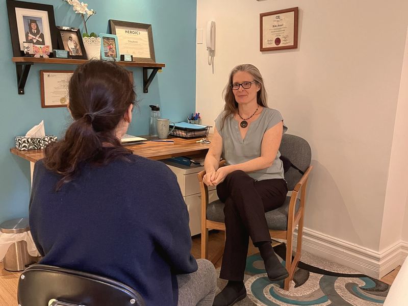 Alida Farrell, seated in her office with the turquoise wall, listening to a person seated across from her