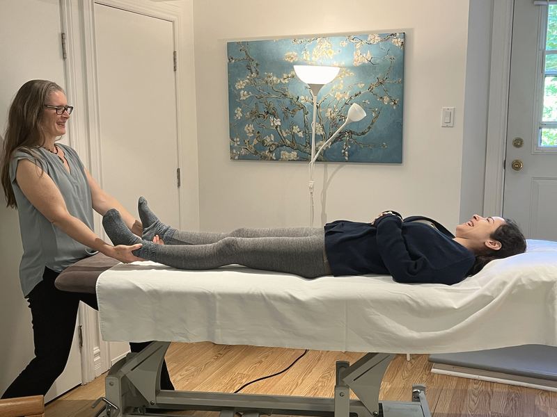 Alida Farrell holding the feet of a person lying on the treatment table, a canvas of almond blossoms on the wall