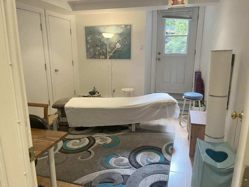 A bright treatment room: the table, a canvas on the wall and the glass door onto the greenery