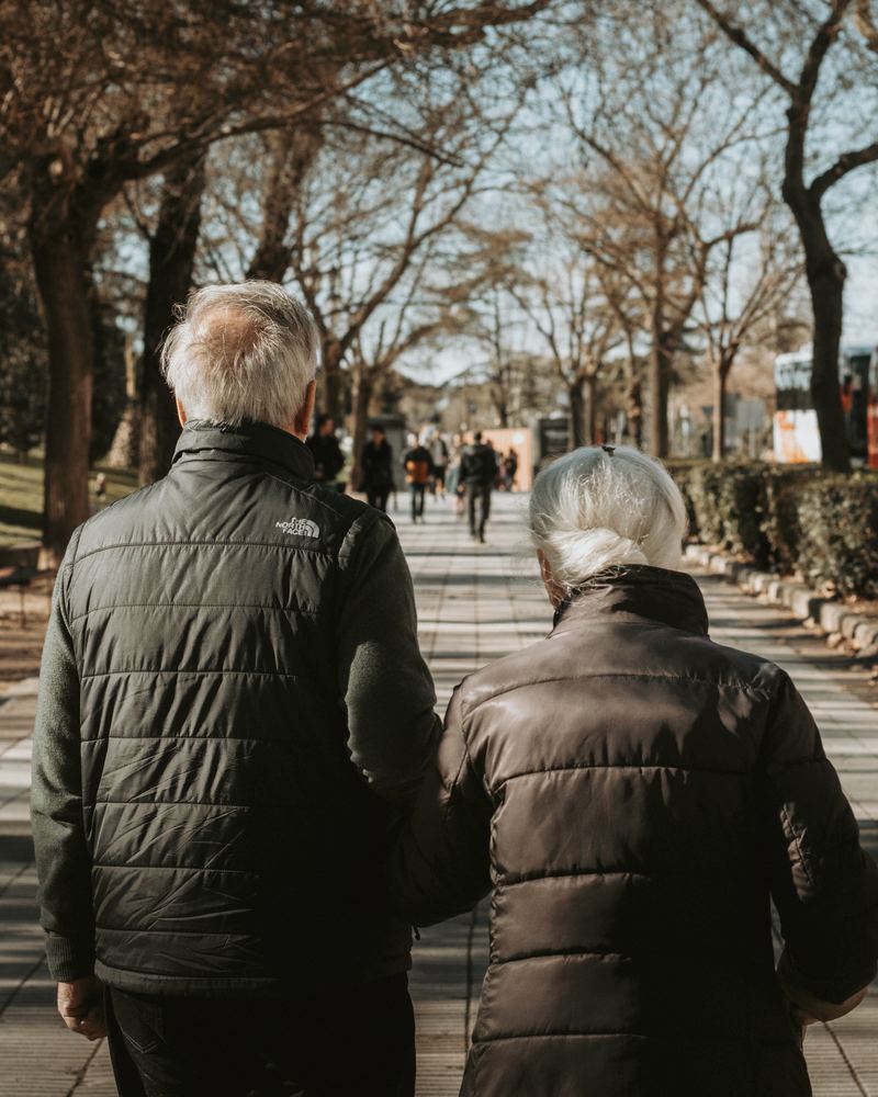 Un couple d'aînés qui marche dans un parc, vu de dos, image d'ambiance