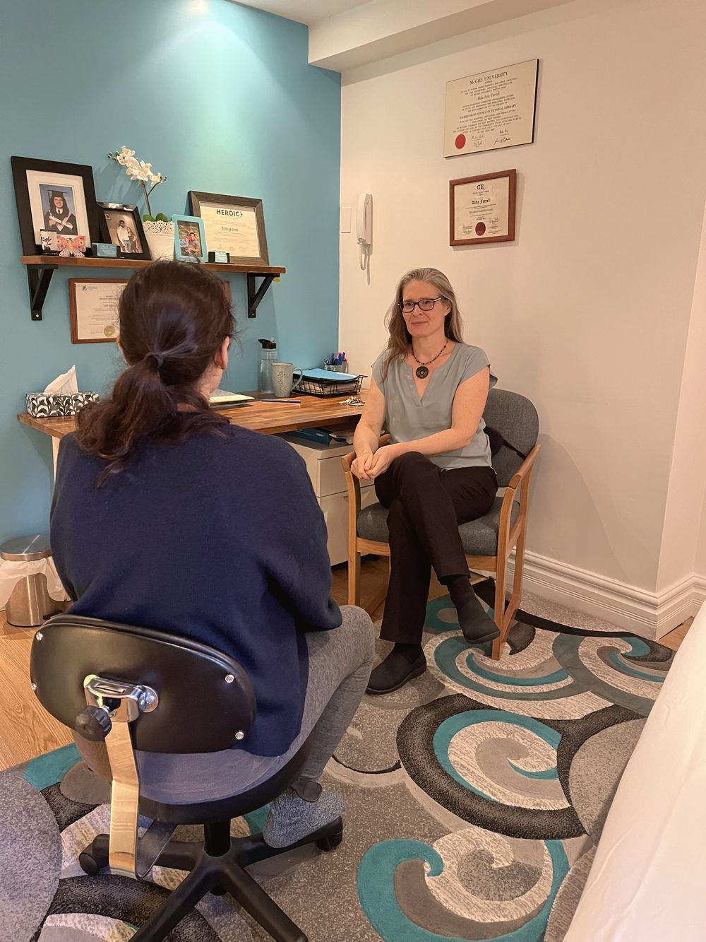 Alida Farrell, assise dans son bureau au mur turquoise, qui écoute une personne assise devant elle