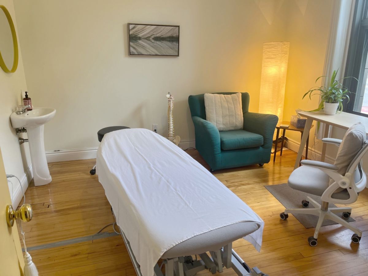 Une salle de traitement lumineuse : une table sous un drap blanc, un fauteuil vert, une lampe de papier et une grande fenêtre