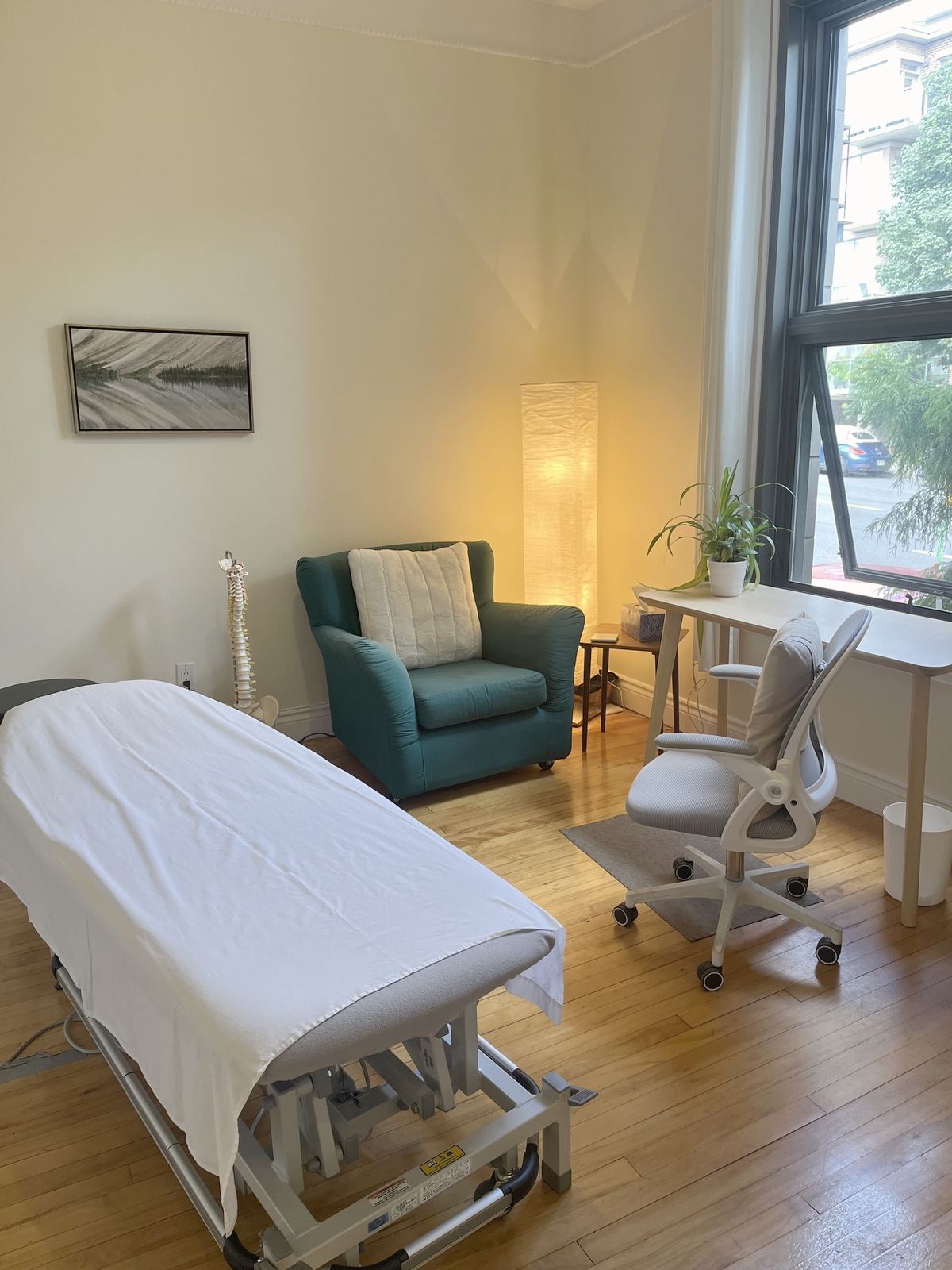Une salle de traitement lumineuse, un fauteuil vert, une lampe de papier, un bureau blanc et une grande fenêtre sur la rue