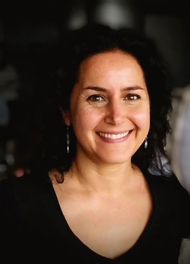 Sharonne Cohen qui sourit, cheveux bouclés et chandail noir, sur un fond sombre