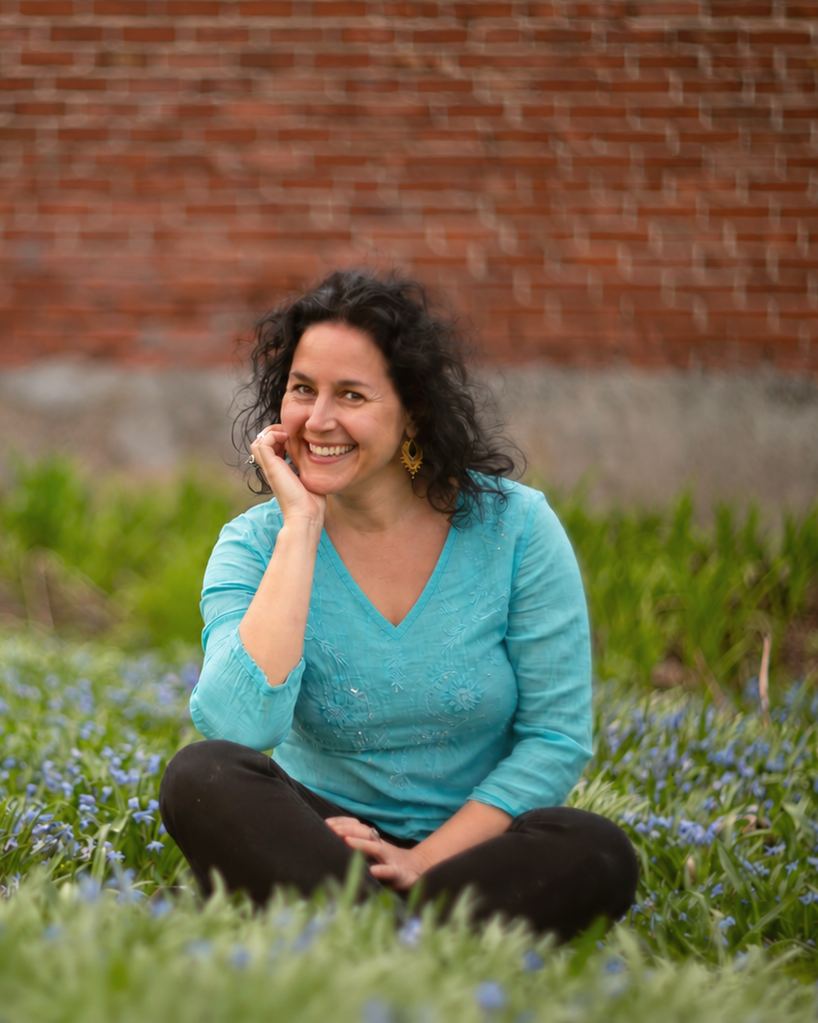 Sharonne Cohen, assise dans l'herbe parmi des fleurs, qui rit