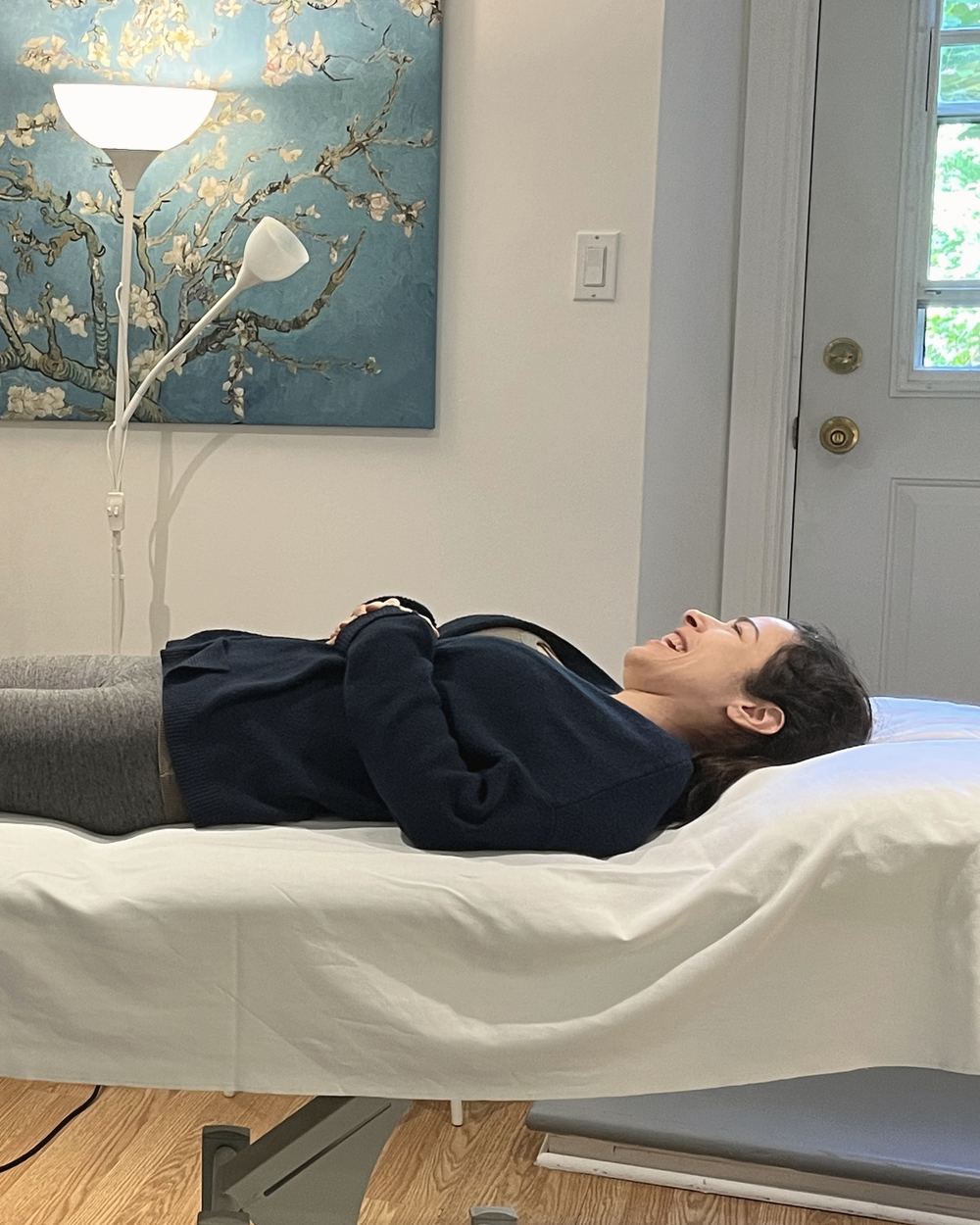 A person lying on the treatment table, smiling, under a canvas of almond blossoms