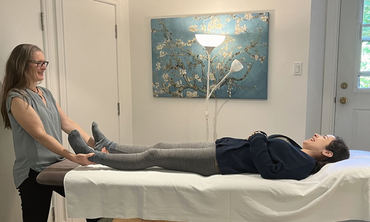 Alida Farrell tient les deux pieds d'une personne allongée sur la table de traitement, une toile d'amandier en fleurs au mur